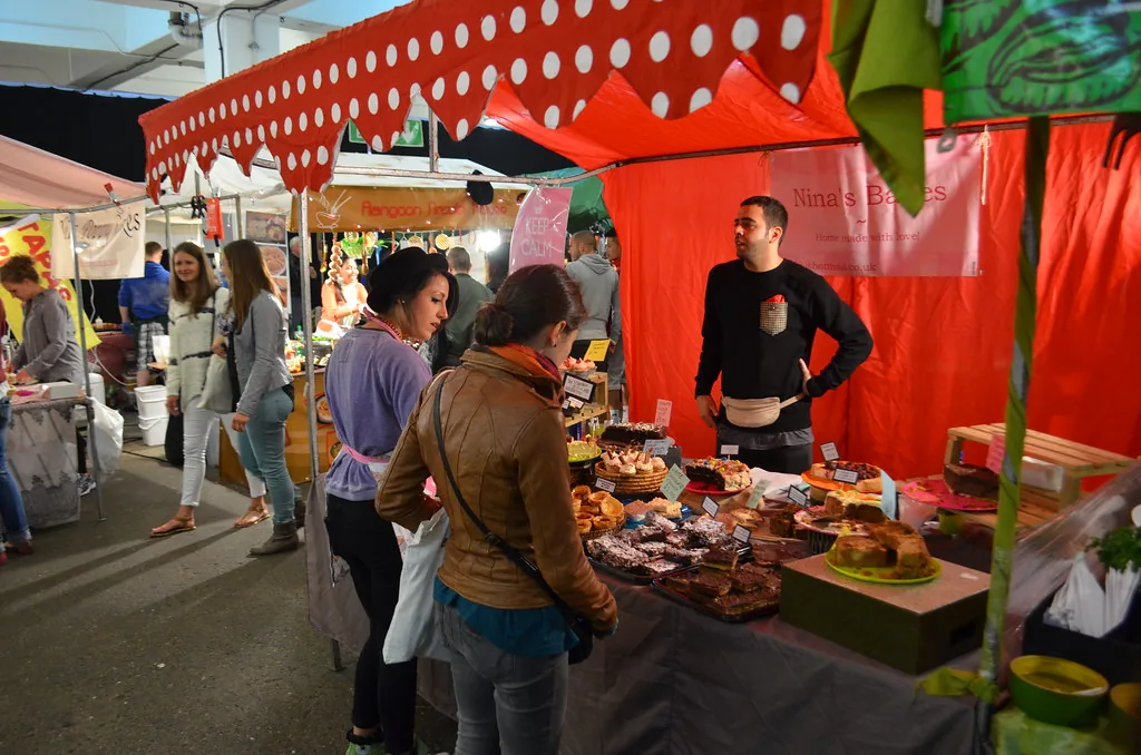Shoppers browsing a street food and baked goods stall at Brick Lane Market
