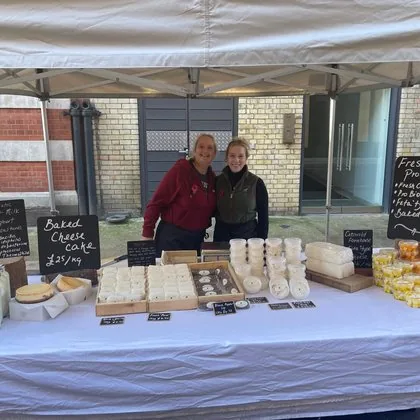 Cheese stall with vendors and chalkboard price signs at Notting Hill Farmers' Market